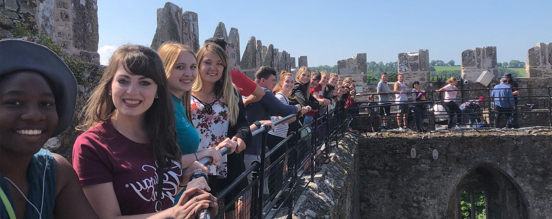 Students line up by the railing of an old stone building.