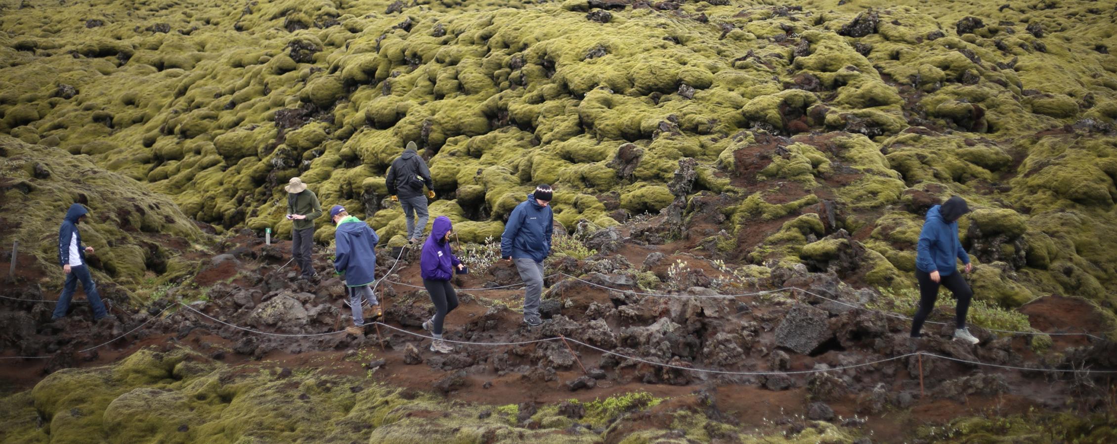 Students walk on a path of rugged terrain.