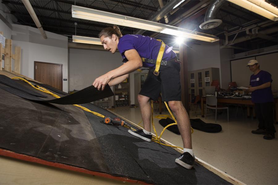 A student climbs on a mock roof during a roofing simulation.