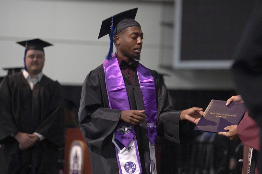 A student accepts their diploma as they walk across the stage at graduation.