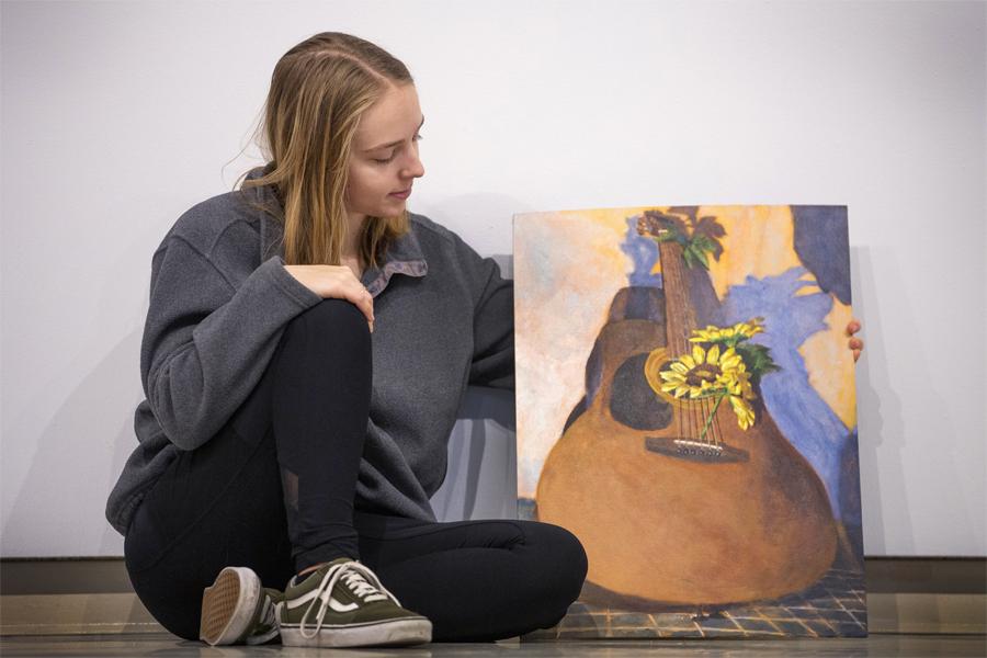 Emma Siskoff sits next to a painting of a guitar.