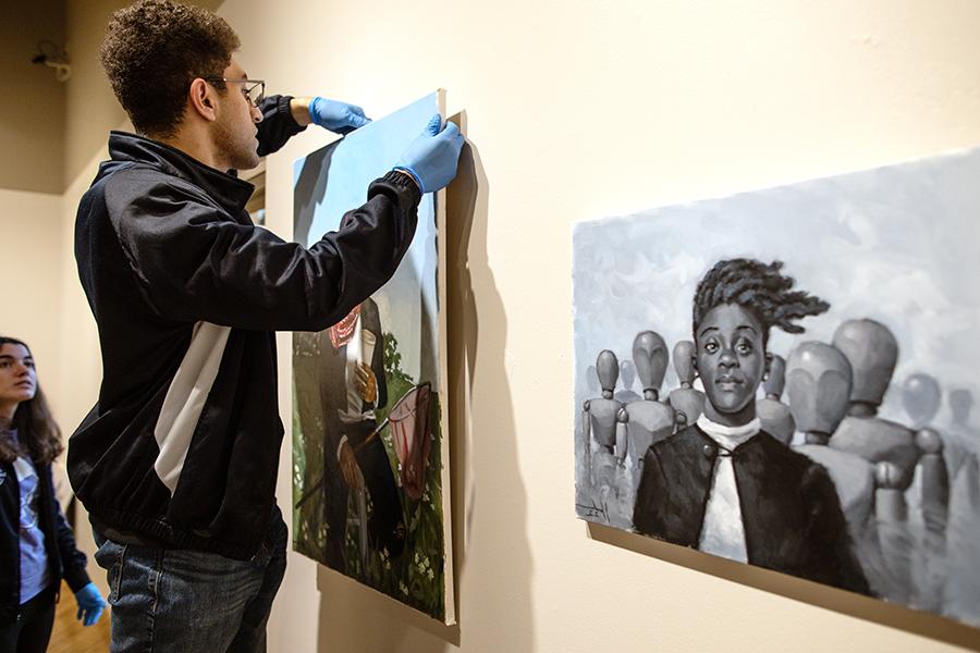 Student hangs art in a gallery with a digital art calculator.