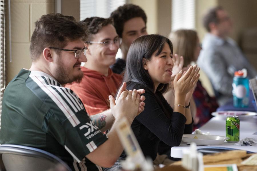 People sitting at table clap and smile.